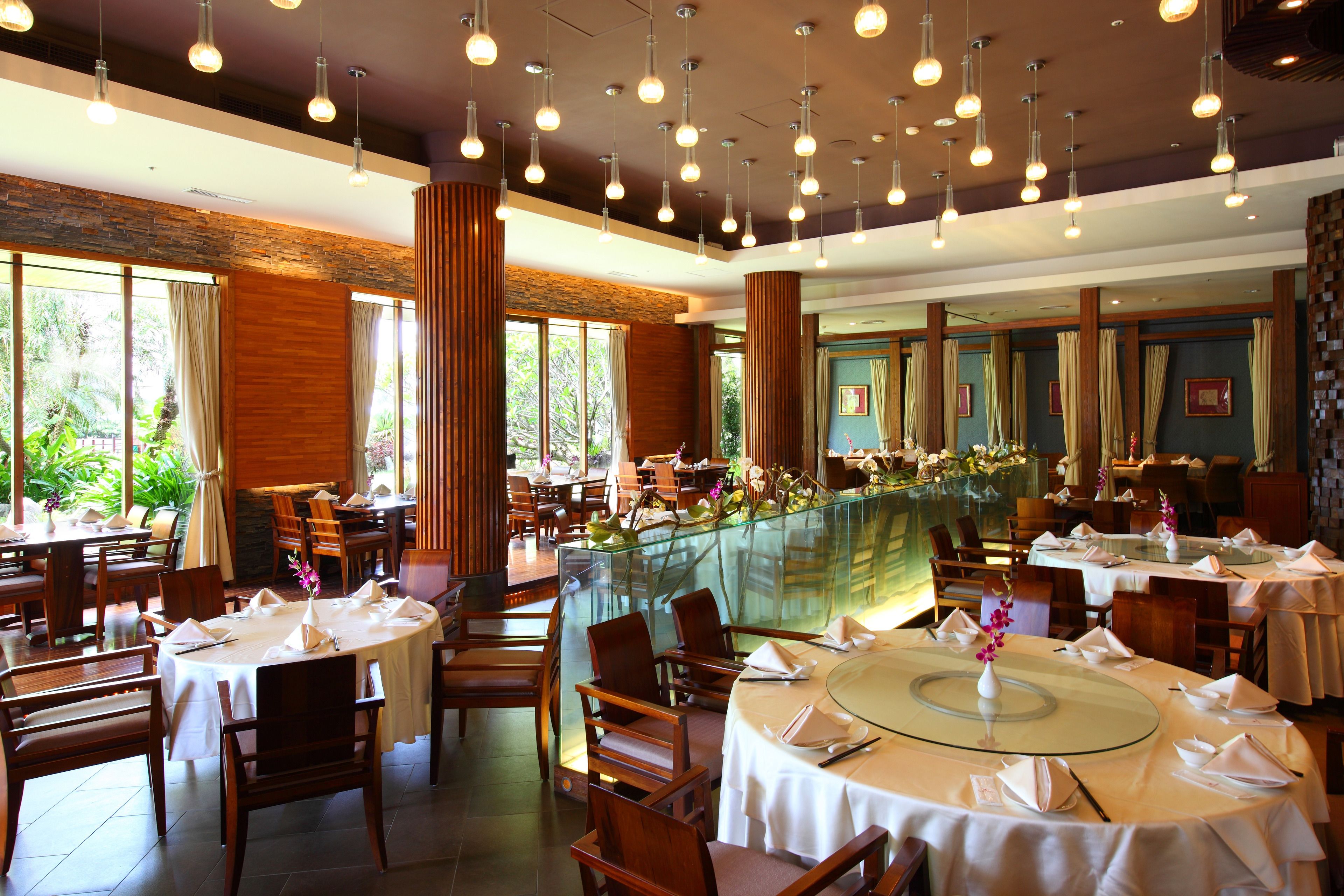 Un restaurante con mesas redondas, sillas de madera y lámparas colgantes.