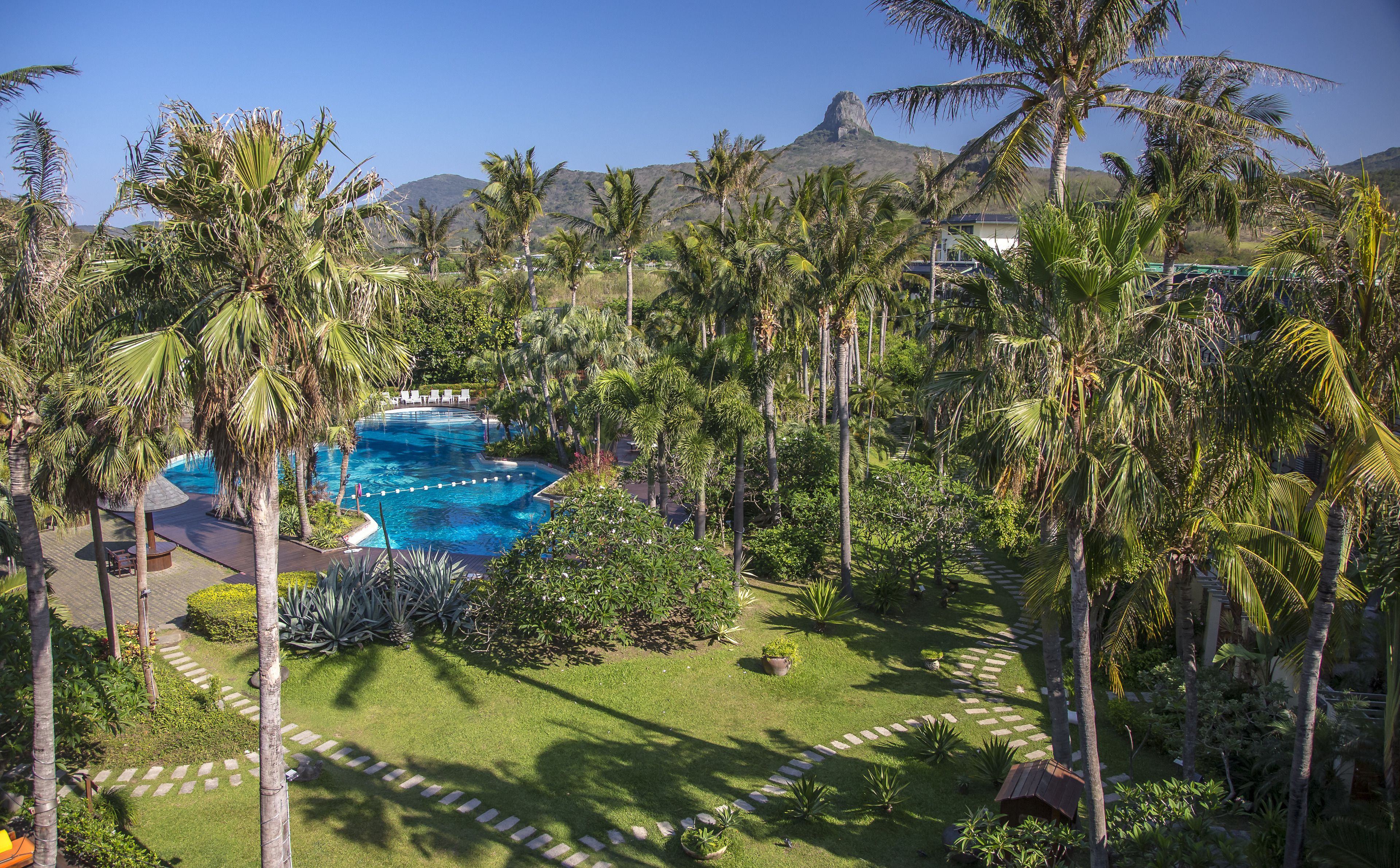 Un complexe hôtelier doté d’une piscine entourée de palmiers, avec une chaîne de montagnes en toile de fond.