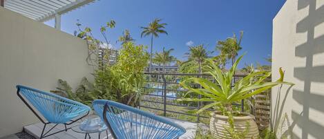 A patio with two blue chairs and a table, surrounded by greenery and a view of a pool.