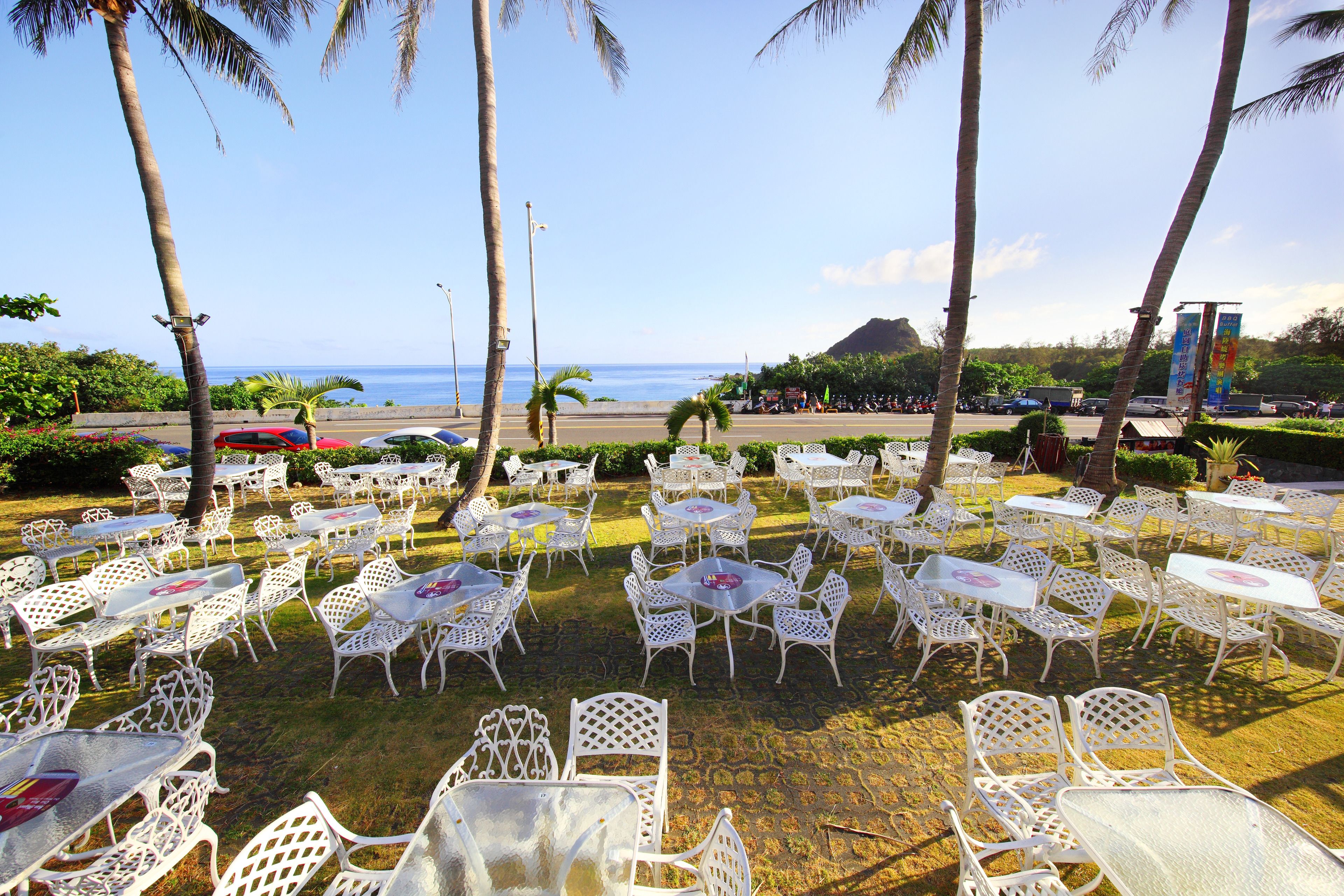 Outdoor seating with tables and chairs arranged on grass, overlooking a beach and ocean.
