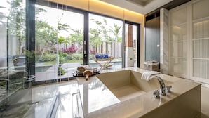 A modern bathroom with a large bathtub, a glass shower enclosure, and a view of a garden. - Caesar Park Kenting (Hengchun)