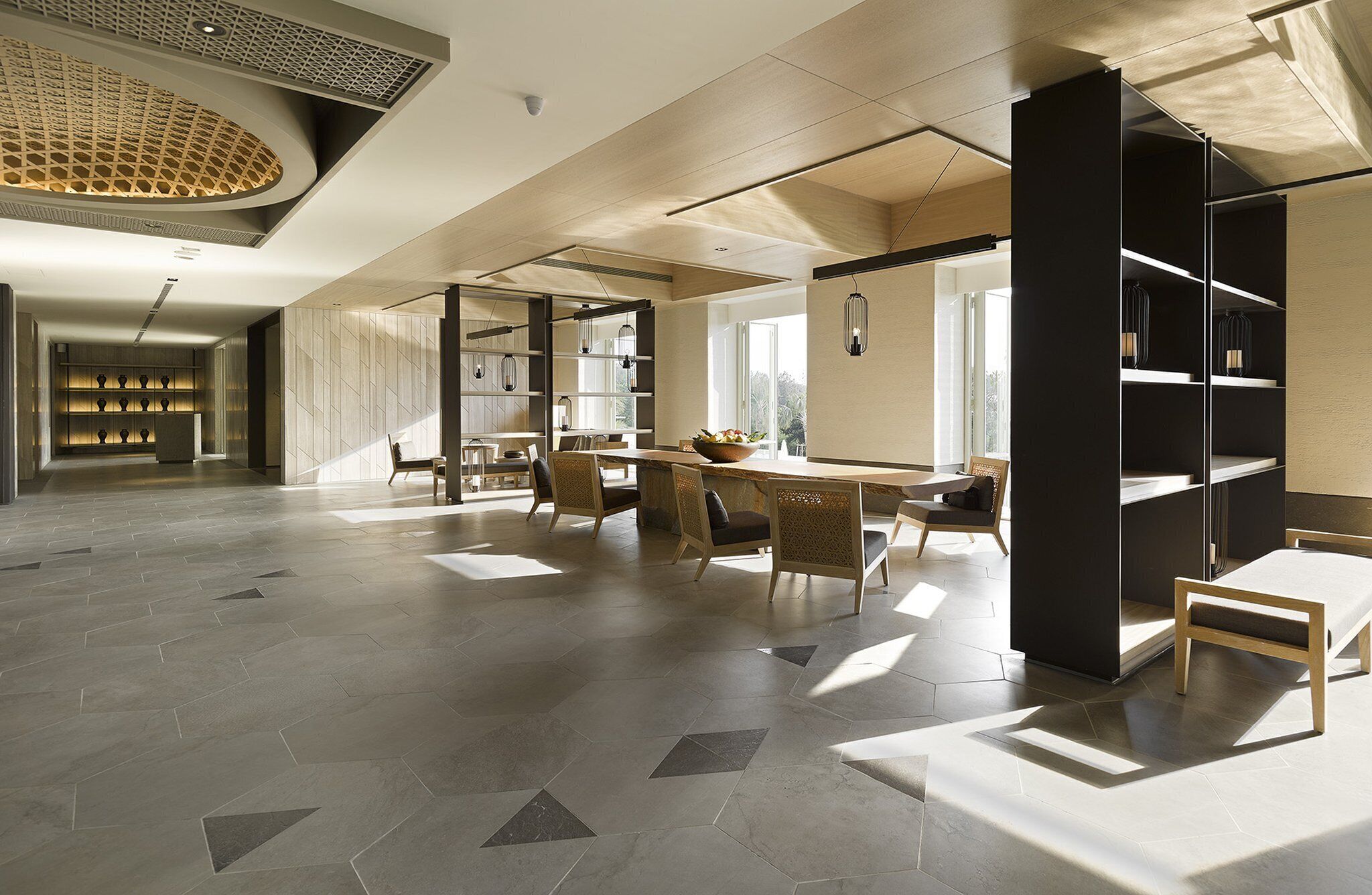 A spacious library with modern furniture, large windows, and a geometric floor pattern.