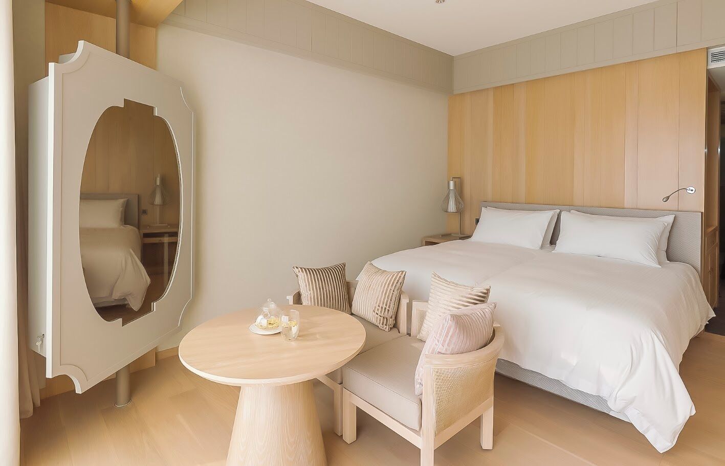 A hotel room with a large bed, a round table with chairs, a mirror, and a bedside lamp.