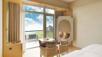 A hotel room with a large bed, a round table with chairs, a large mirror, and a view of a mountainous landscape through the windows.