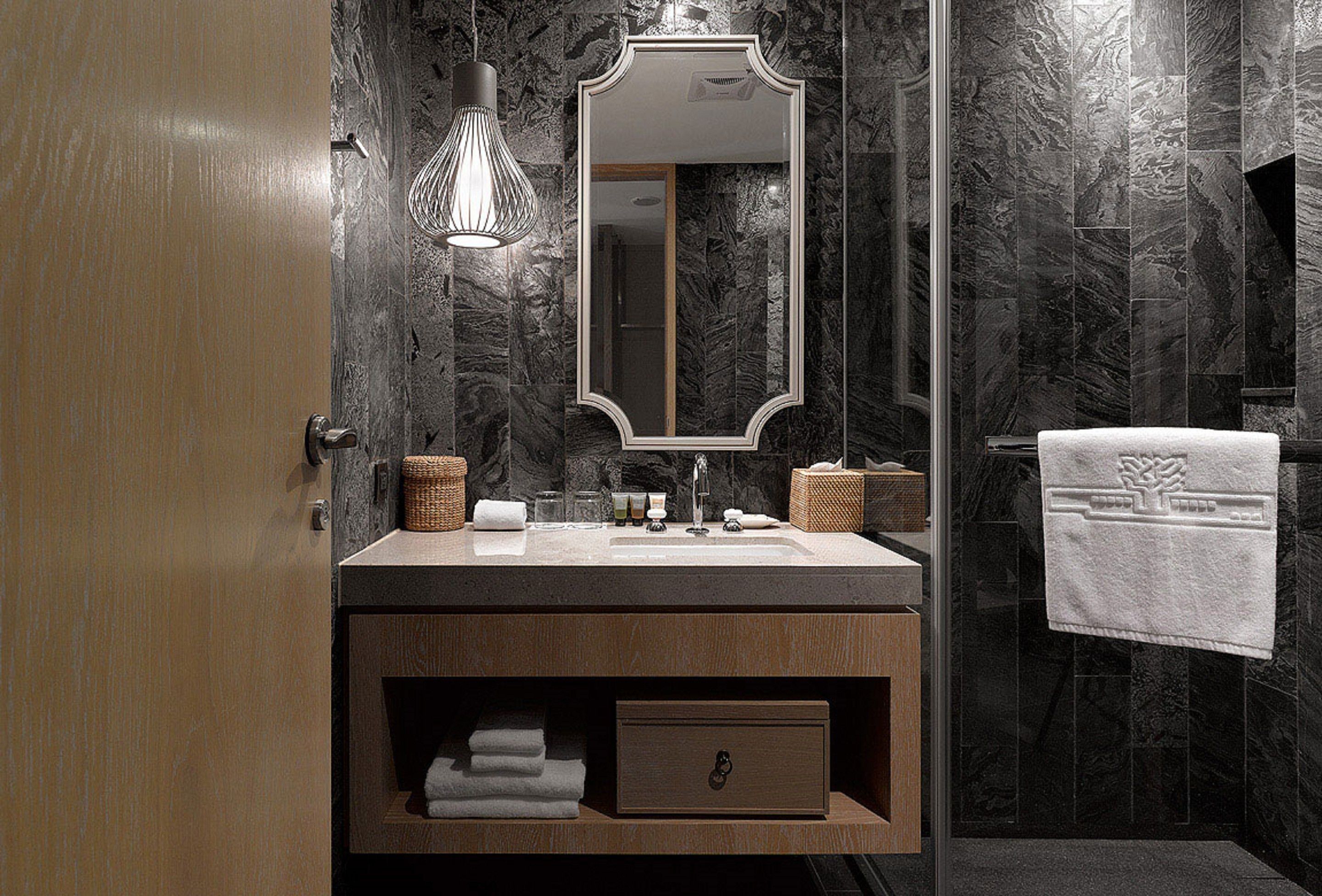 Un baño moderno con pared de mármol, tocador de madera, espejo grande y una toalla colgada en la pared.
