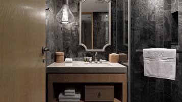Un baño moderno con pared de mármol, tocador de madera, espejo grande y una toalla colgada en la pared.