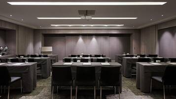 A conference room with multiple tables and chairs, equipped with projectors and a large screen.