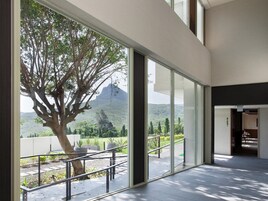 Un edificio moderno con amplios ventanales que ofrecen vista a un árbol y colinas distantes.