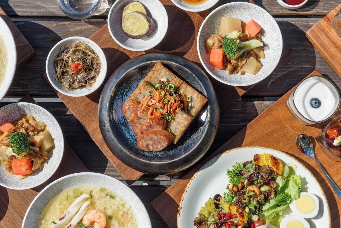 Verschiedene Gerichte auf einem Holztisch, darunter eine Suppenschale, ein Salat und weitere Teller mit Gemüse und Fleisch.