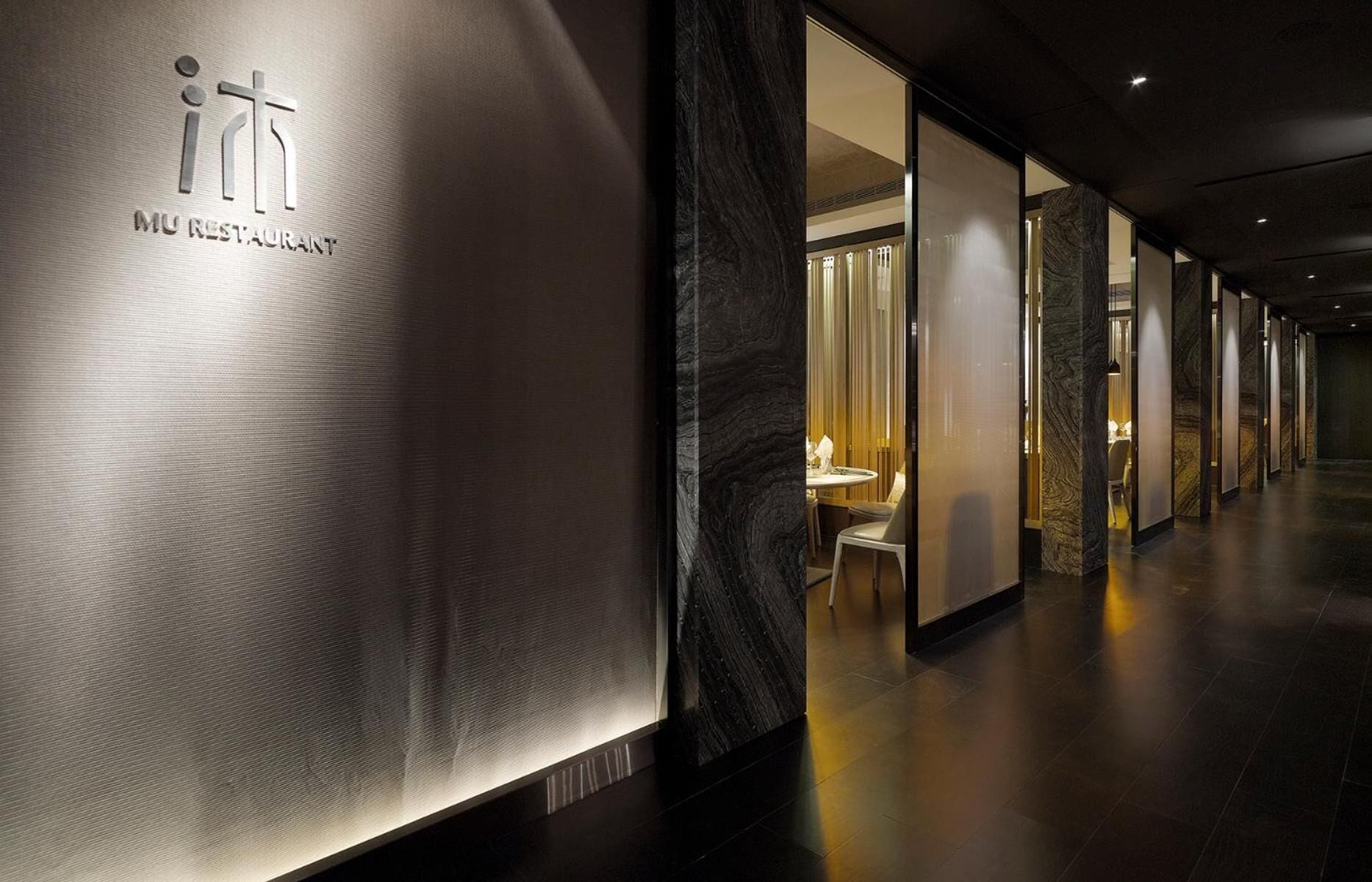 A modern hotel corridor with a metallic wall featuring the logo and name of the hotel.