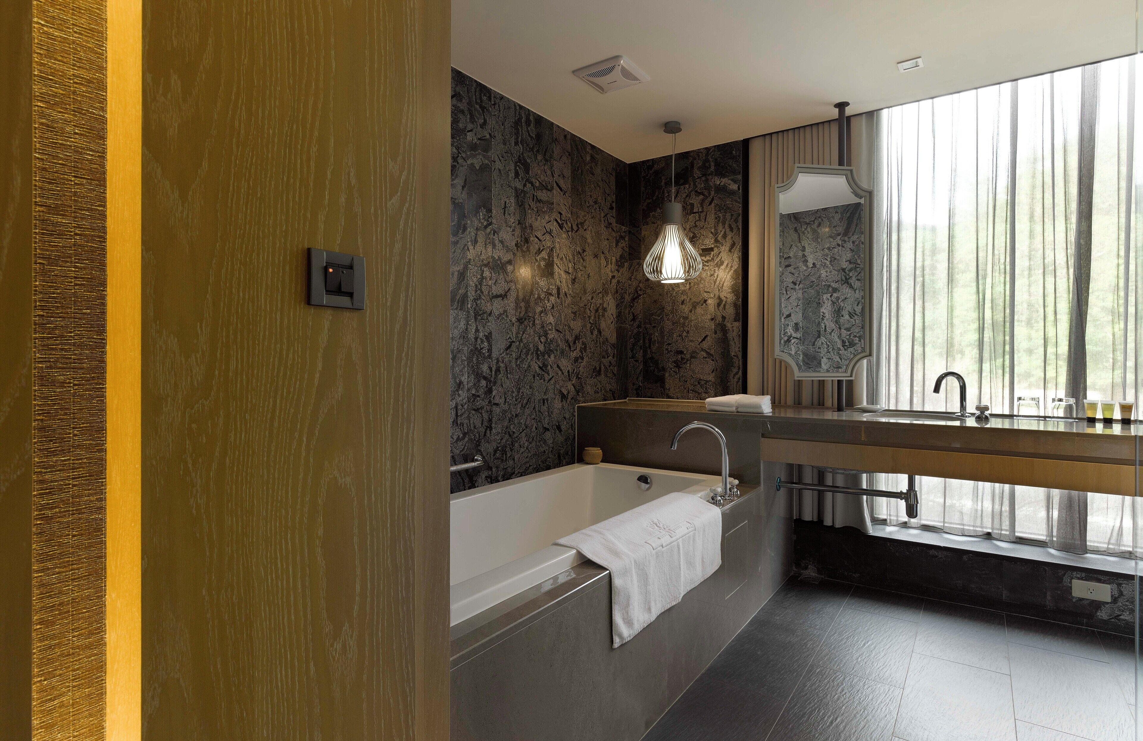 A modern bathroom with a bathtub, a vanity with a mirror, and a window with curtains.