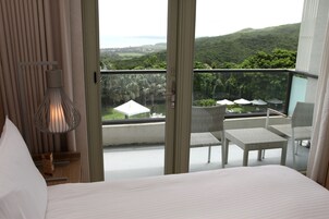 Un dormitorio con balcón que ofrece vistas a un paisaje exuberante y al mar.