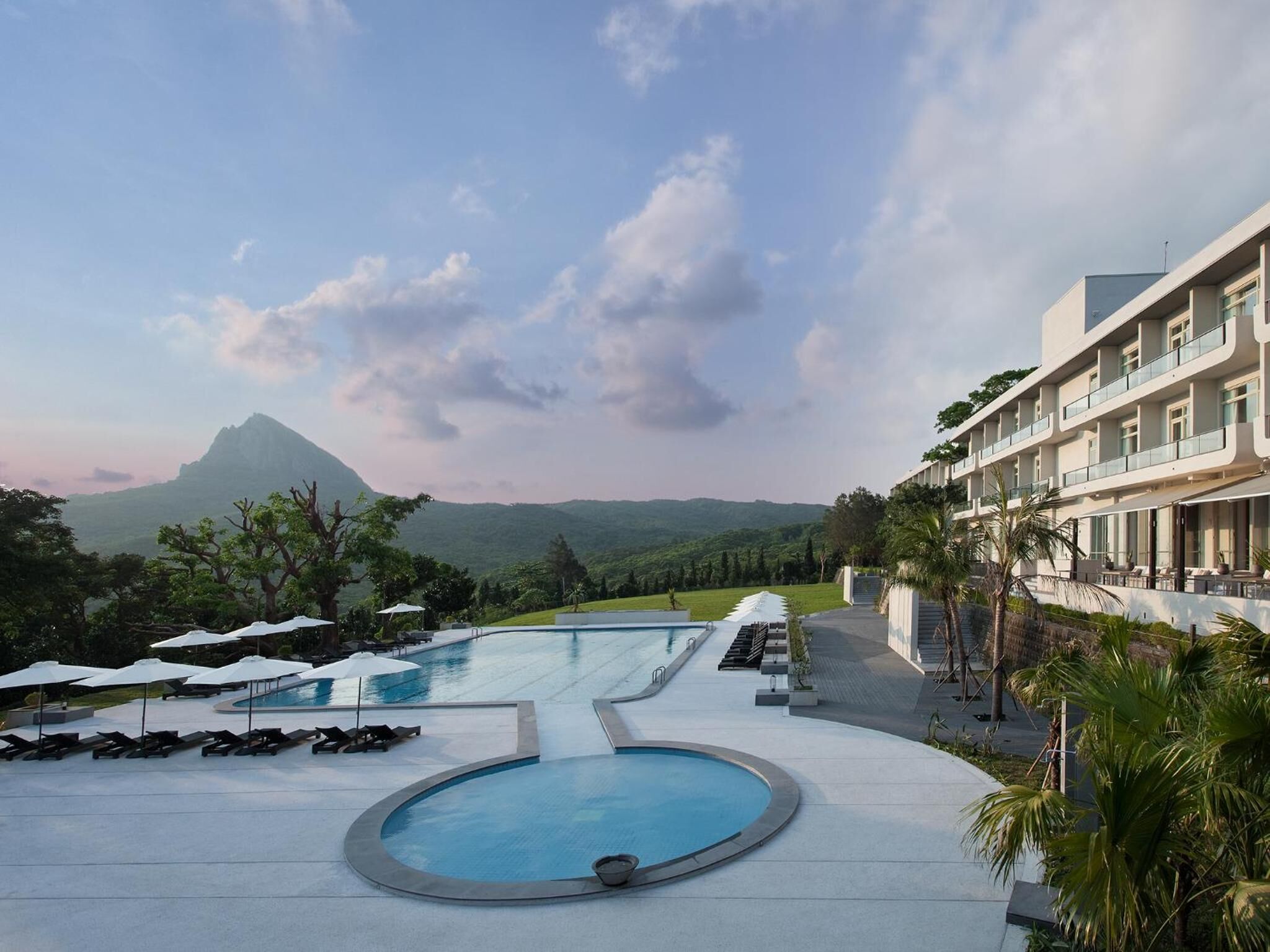 A resort with a swimming pool, lounge chairs, and a view of a mountain.