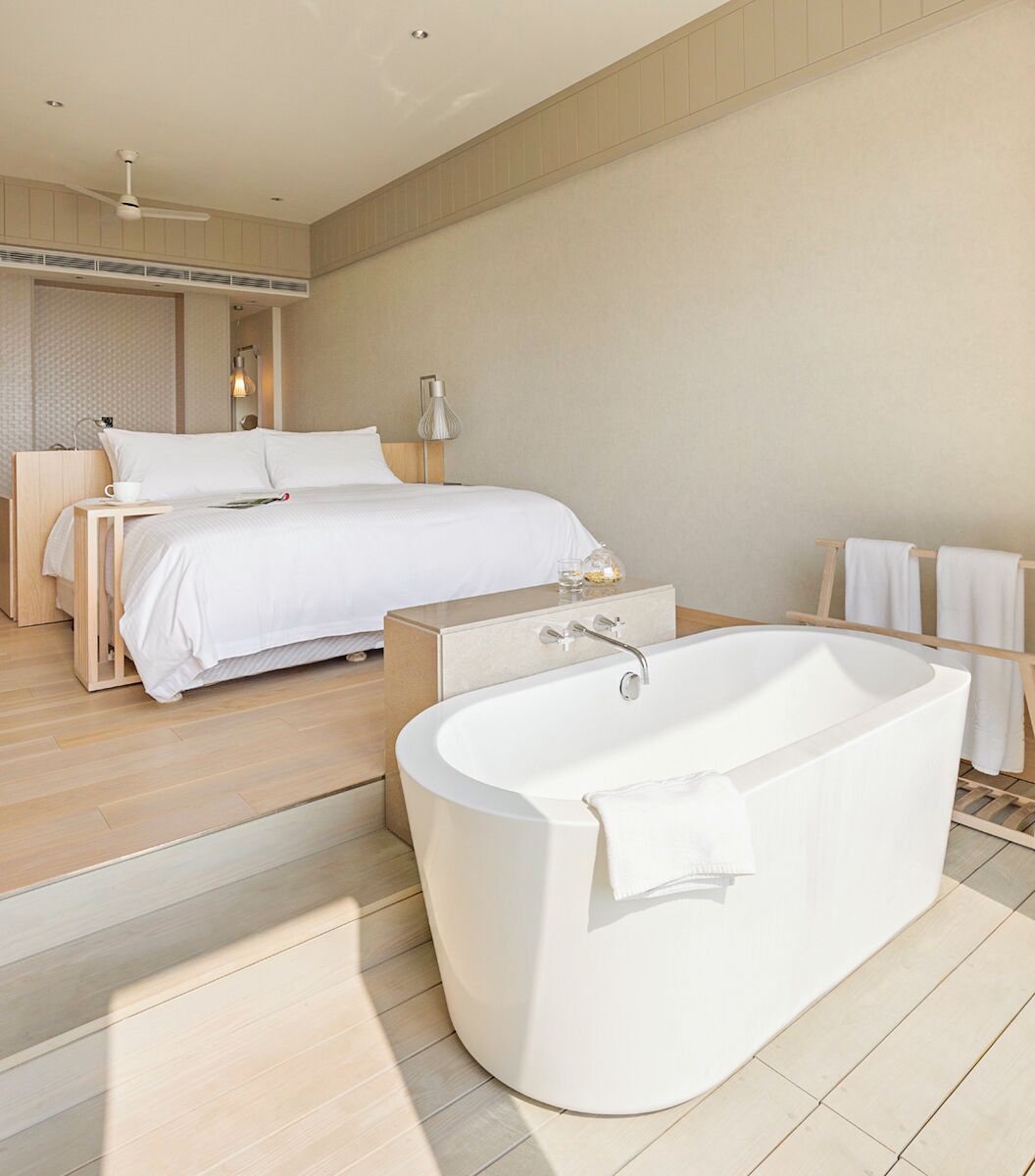 A modern bedroom with a large bed, a freestanding bathtub, and a nightstand with a cup and glass.