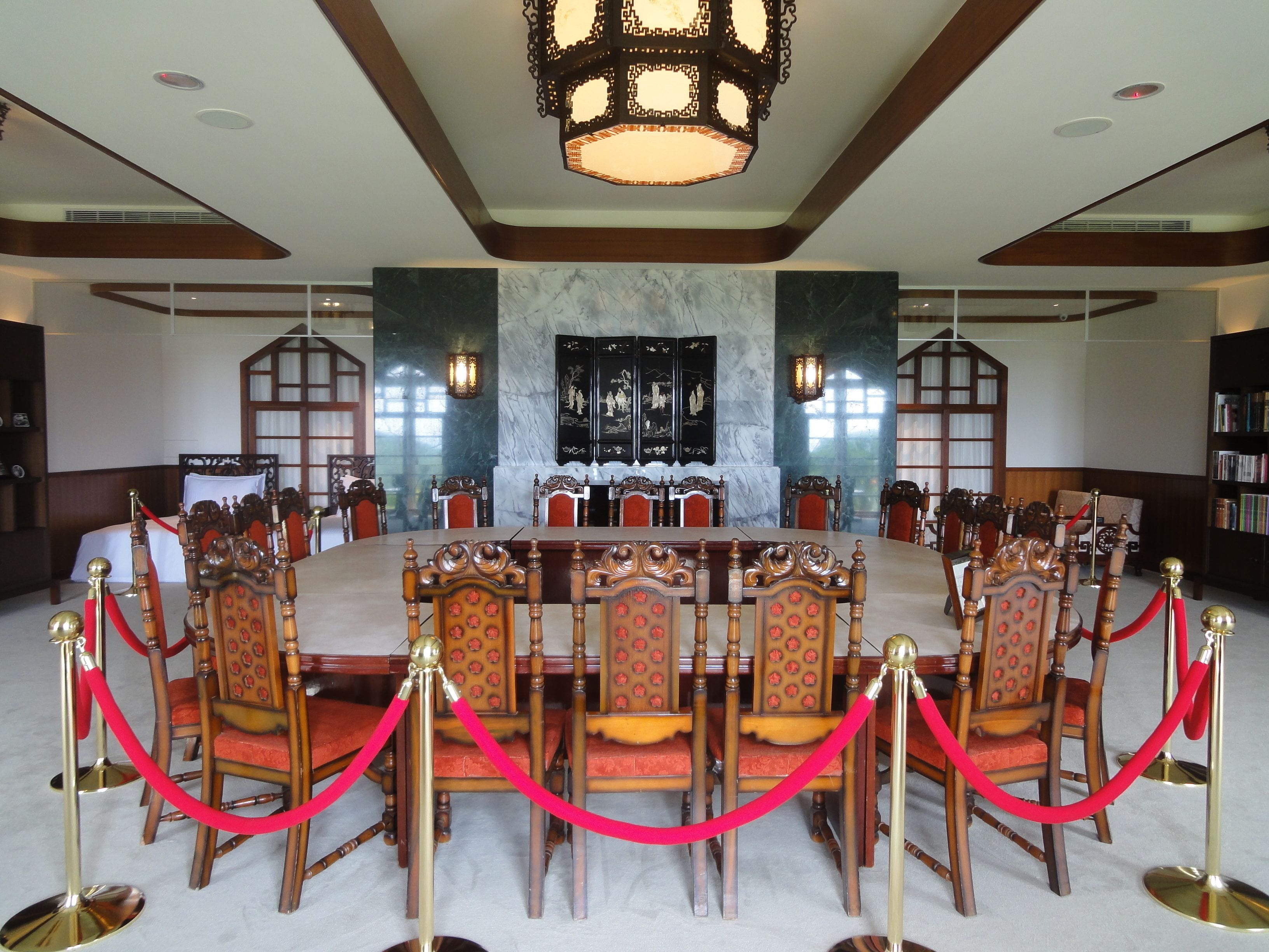 A formal meeting room with a large oval table, red velvet ropes, and ornate chairs.
