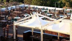 A coastal view with a rocky outcrop in the sea, a restaurant area with outdoor seating, and a hilly landscape in the background. - Fullon Resort Kending (Hengchun)