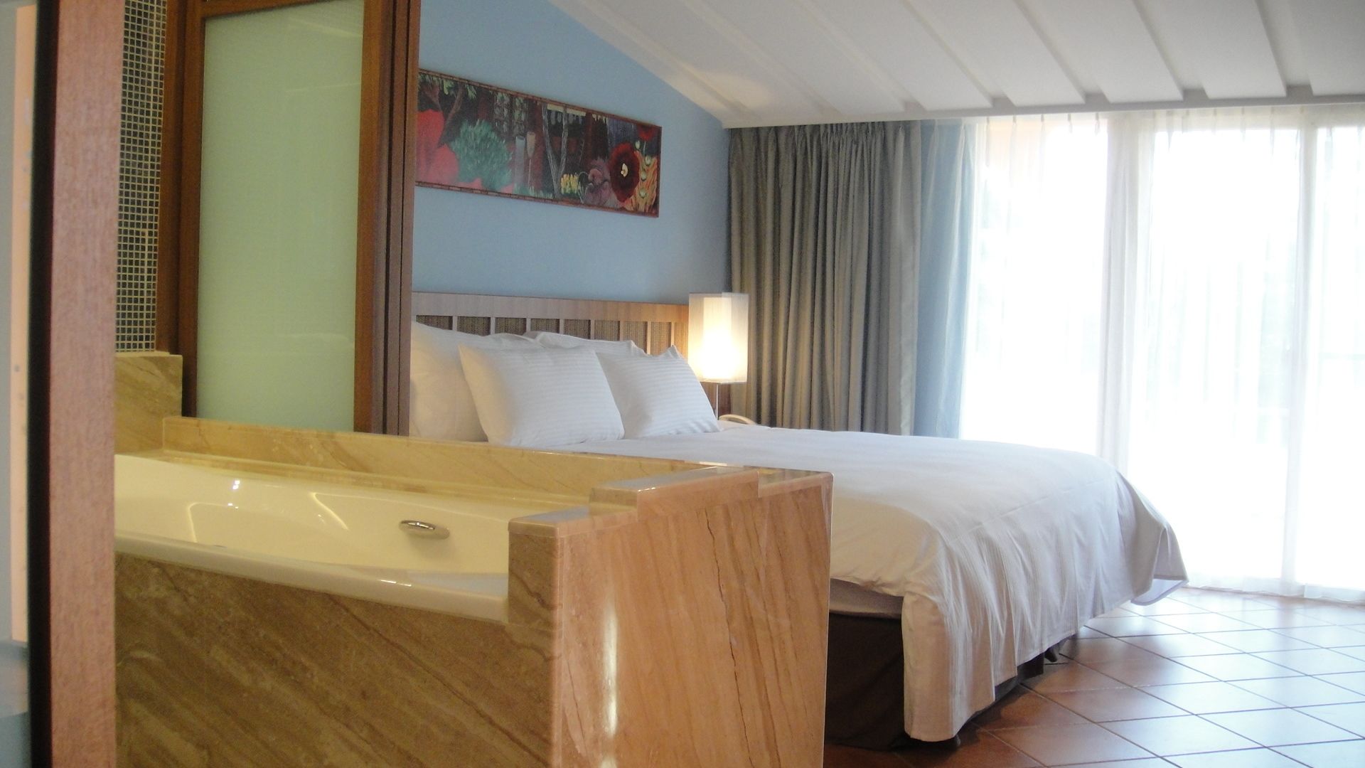 Habitación de hotel con una cama grande, una bañera, un cuadro en la pared y una ventana con cortinas.