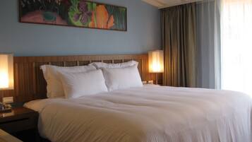 A hotel room with a large bed, two bedside lamps, a wooden headboard, and a floral painting on the wall.
