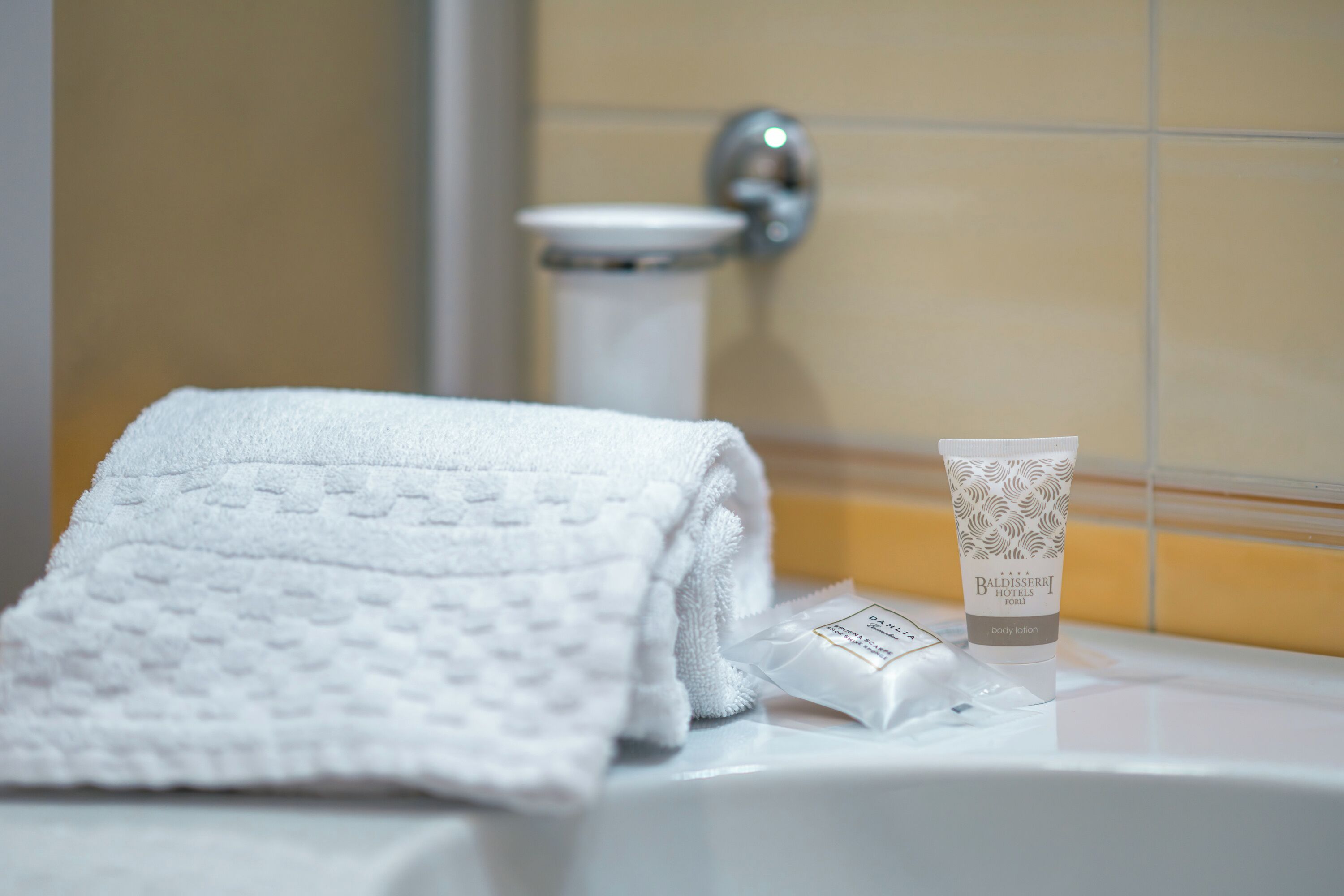 A bathroom with a white towel, a bottle of body lotion, and a toilet.