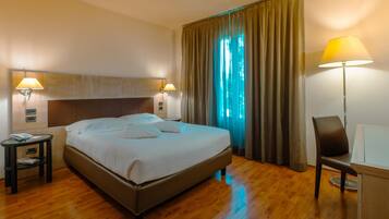 Una camera d'albergo con un letto, lampade sui comodini, una scrivania e una sedia.