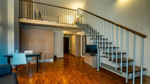 Un vaste espace de vie doté d’un plancher en bois, d’une table à manger avec des chaises, d’un canapé, d’un téléviseur et d’un escalier muni d’une rampe.