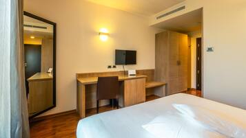 Una camera d'albergo con un letto, una scrivania, una sedia, uno specchio, una TV a parete e una porta.