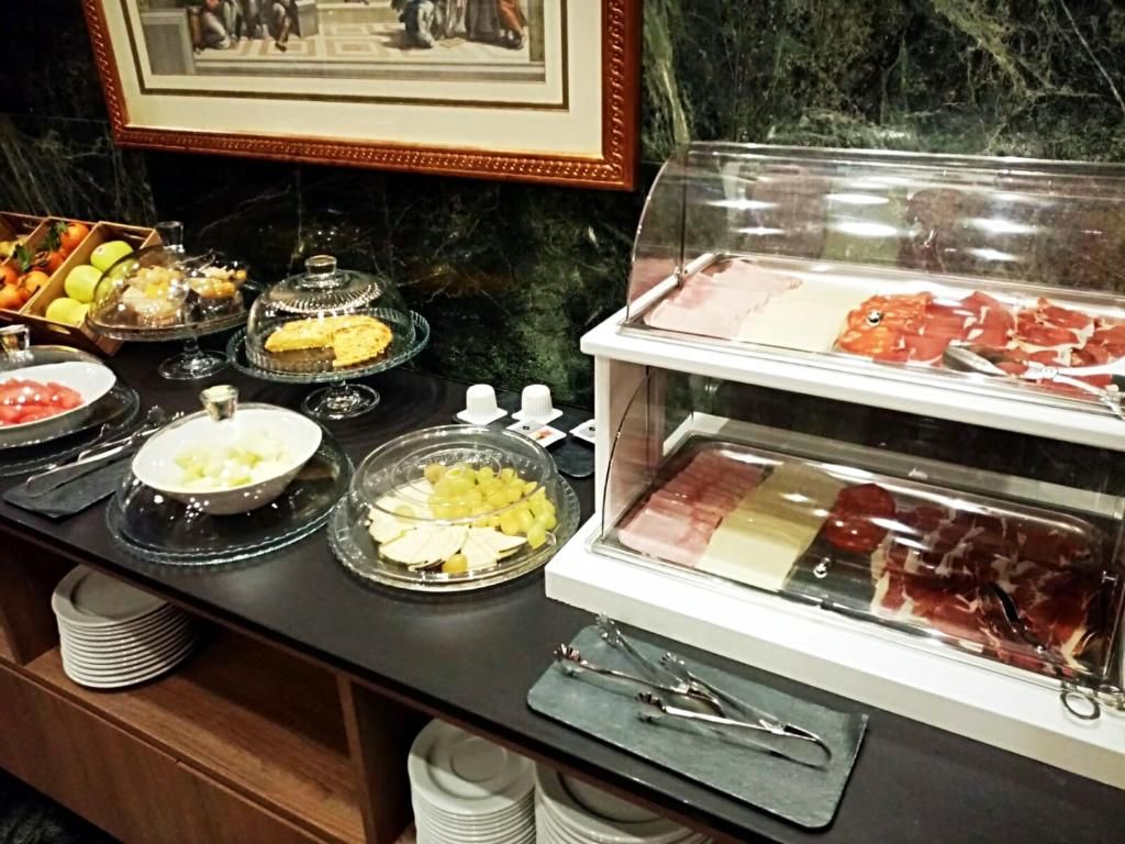 Tarjolla on runsas buffet, jossa on monenlaisia ruokia, kuten hedelmiä, juustoja ja lihatuotteita, ja ne on esillä lasiastioissa ja vitriinissä.