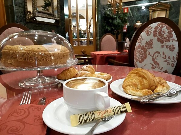 A dining table with a dessert display, a cup of coffee, croissants, and a chocolate bar. - Hotel Imperial (Valladolid)