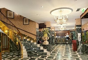 Um saguão de hotel com piso de mármore, uma escadaria imponente e um lustre.