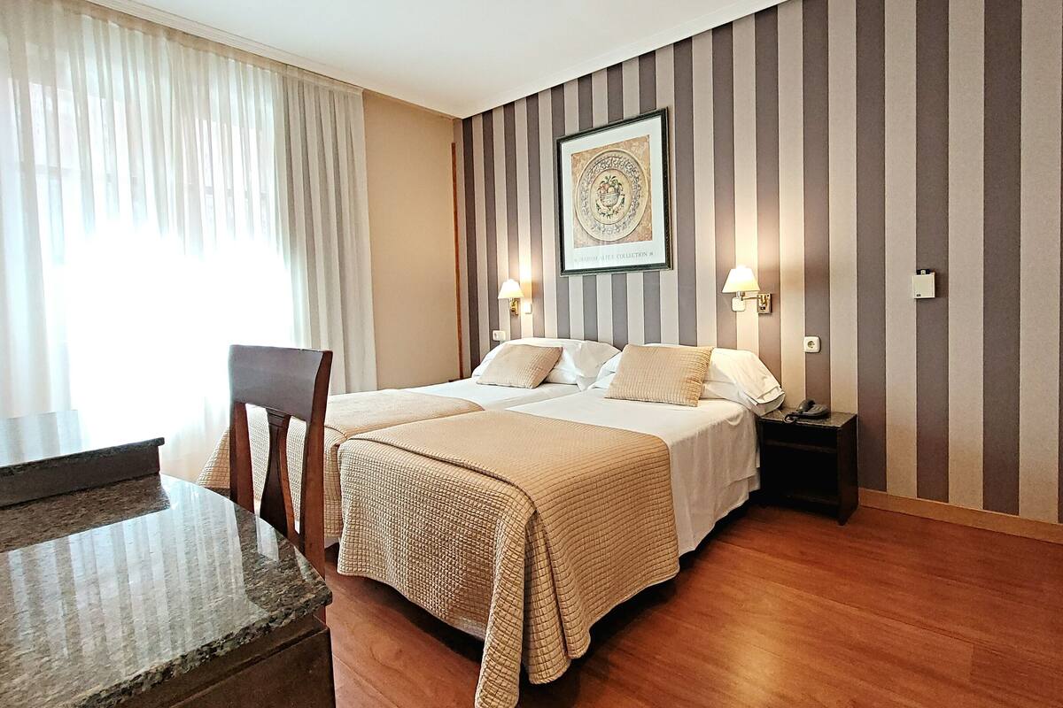 Habitación de hotel con dos camas, una mesa de comedor y una silla. Hay lámparas de pared y un cuadro en la pared.