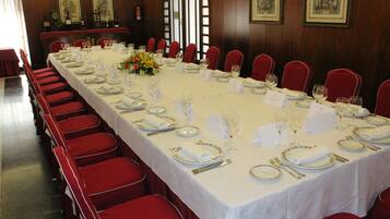Una larga mesa de comedor dispuesta para un evento formal, con sillas rojas, mantel blanco y centros de mesa florales.
