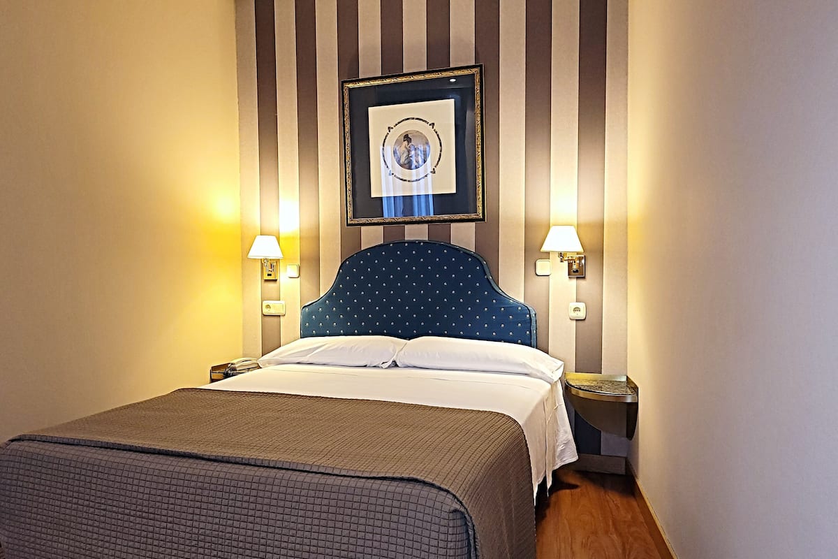 Una habitación de hotel con una cama grande, dos mesitas de noche, un cuadro enmarcado en la pared y dos lámparas de pared.