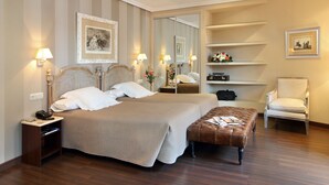 A neatly arranged hotel room with a large bed, bedside tables, a chair, a bench, and a mirror. - Hotel Imperial (Valladolid)