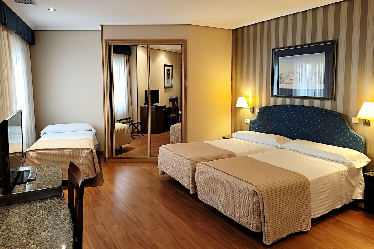 Una habitación de hotel con dos camas, un escritorio, una silla, un televisor y un espejo.