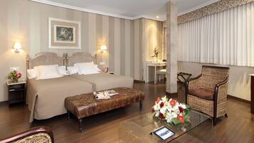 Une chambre d’hôtel avec un grand lit, deux tables de chevet, une table basse en verre, un fauteuil en osier et un bureau avec une chaise.