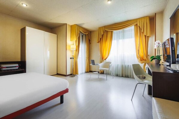A hotel room with a bed, a desk, a chair, and a television.