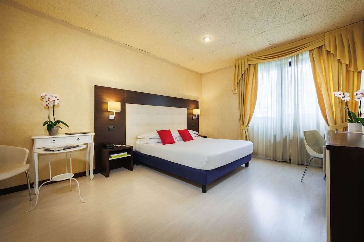 Una habitación de hotel con una cama grande, mesitas de noche, un escritorio y una silla.