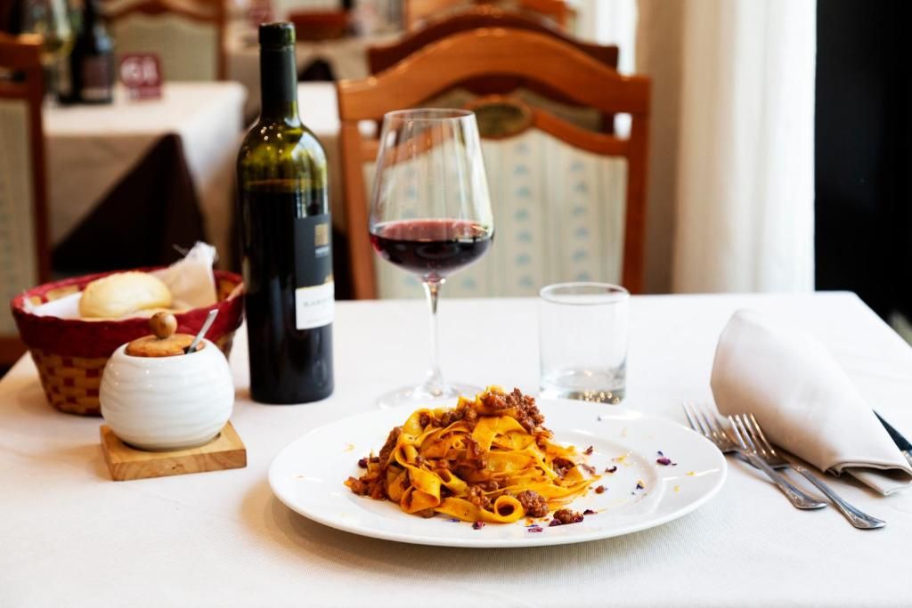 Een eettafel met een bord pasta, een fles wijn, een glas rode wijn en een klein kommetje brood.