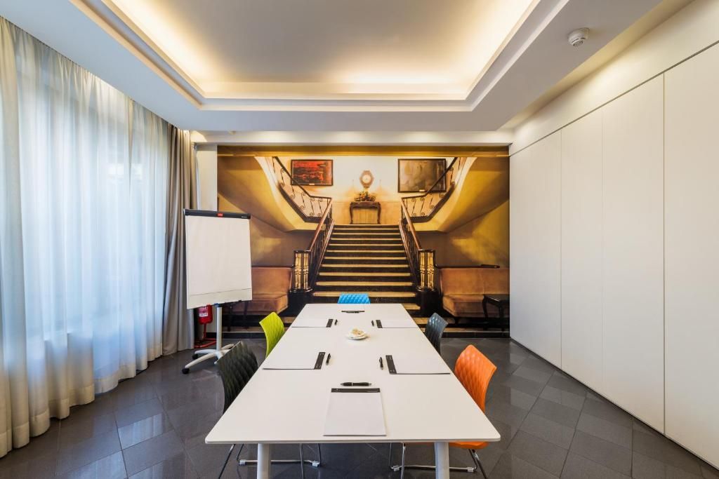 A conference room with a long table, chairs, a whiteboard, and a staircase in the background.