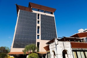 Um edifício alto com design moderno, apresentando uma grande fachada de vidro e um restaurante na base.