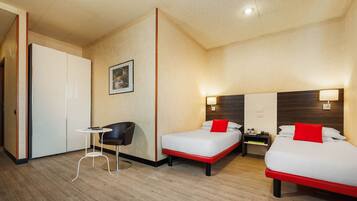 A hotel room with two beds, a small table, a chair, and a wardrobe.