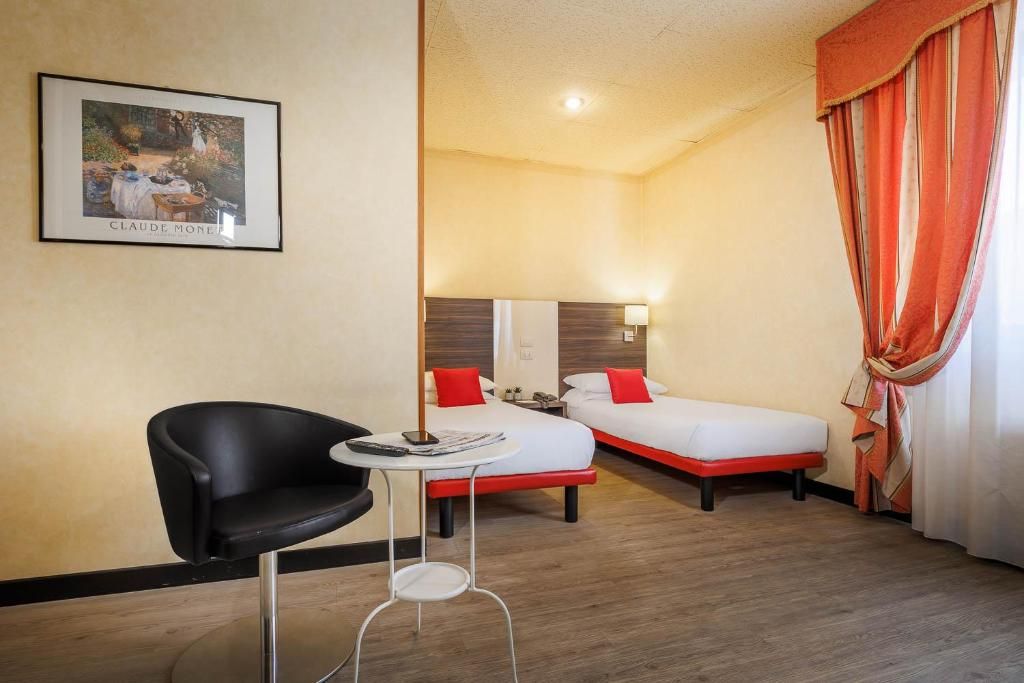 A hotel room with two beds, a small table, a chair, and a framed picture on the wall.