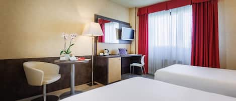 Habitación de hotel con dos camas, un escritorio, una silla, una lámpara y un televisor.