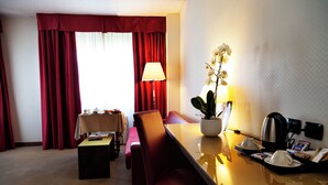 A hotel room with a dining area, a table with a lamp, a potted orchid, and a tray with cups and a coffee maker. - JR Hotels Bologna Amadeus (Bologna)
