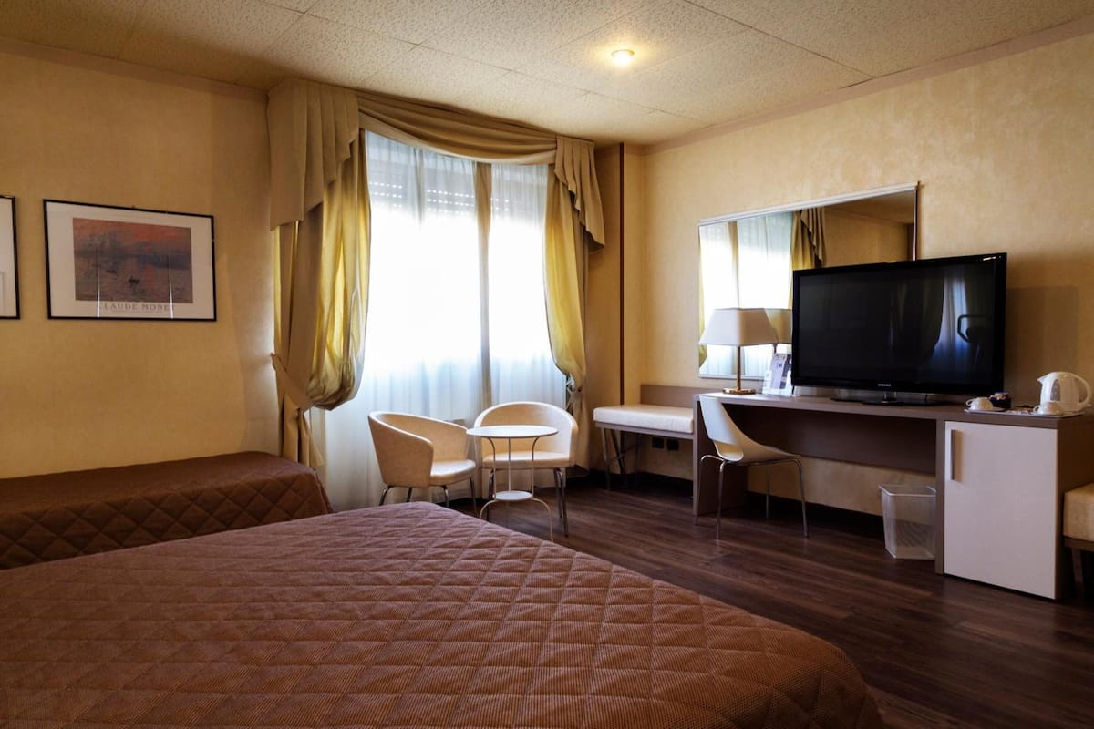 Una habitación de hotel con cama, escritorio, televisión y una silla.
