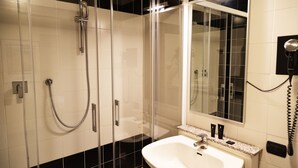 A modern bathroom with a glass-enclosed shower, a white sink with a granite countertop, and a mirror above the sink. - JR Hotels Bologna Amadeus (Bologna)