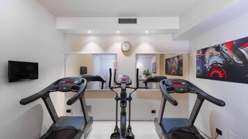 A home gym with two treadmills, a stationary bike, and a wall clock.