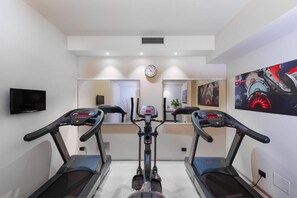 Un gimnasio en casa con dos cintas de correr, una bicicleta estática y un reloj de pared.
