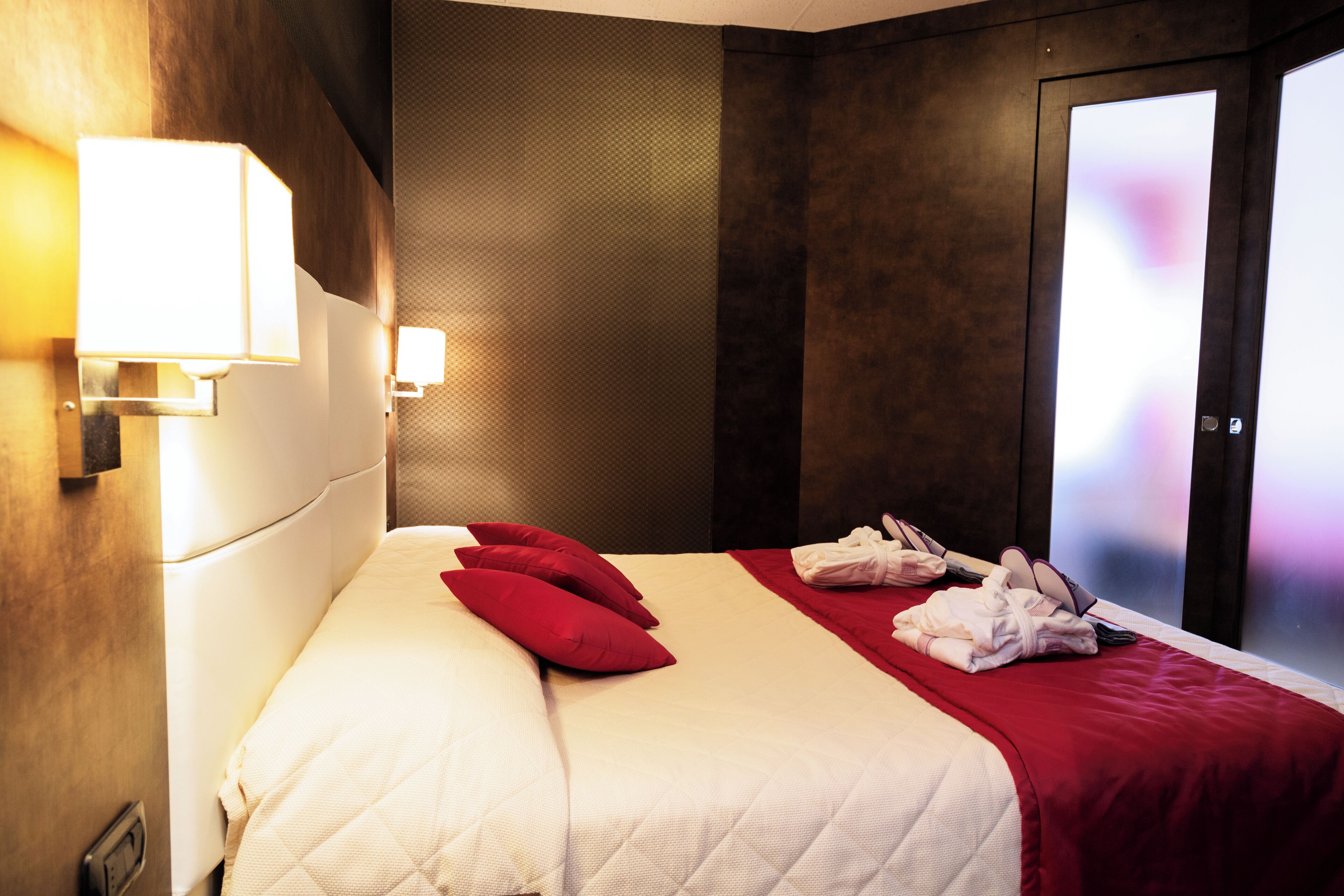 A hotel room with a large bed, red pillows, a red throw blanket, and a set of towels on the bed.