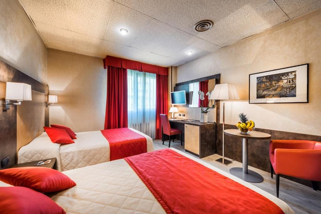 Una camera d'albergo con due letti, una scrivania, una sedia, un televisore e un piccolo tavolo con frutta.